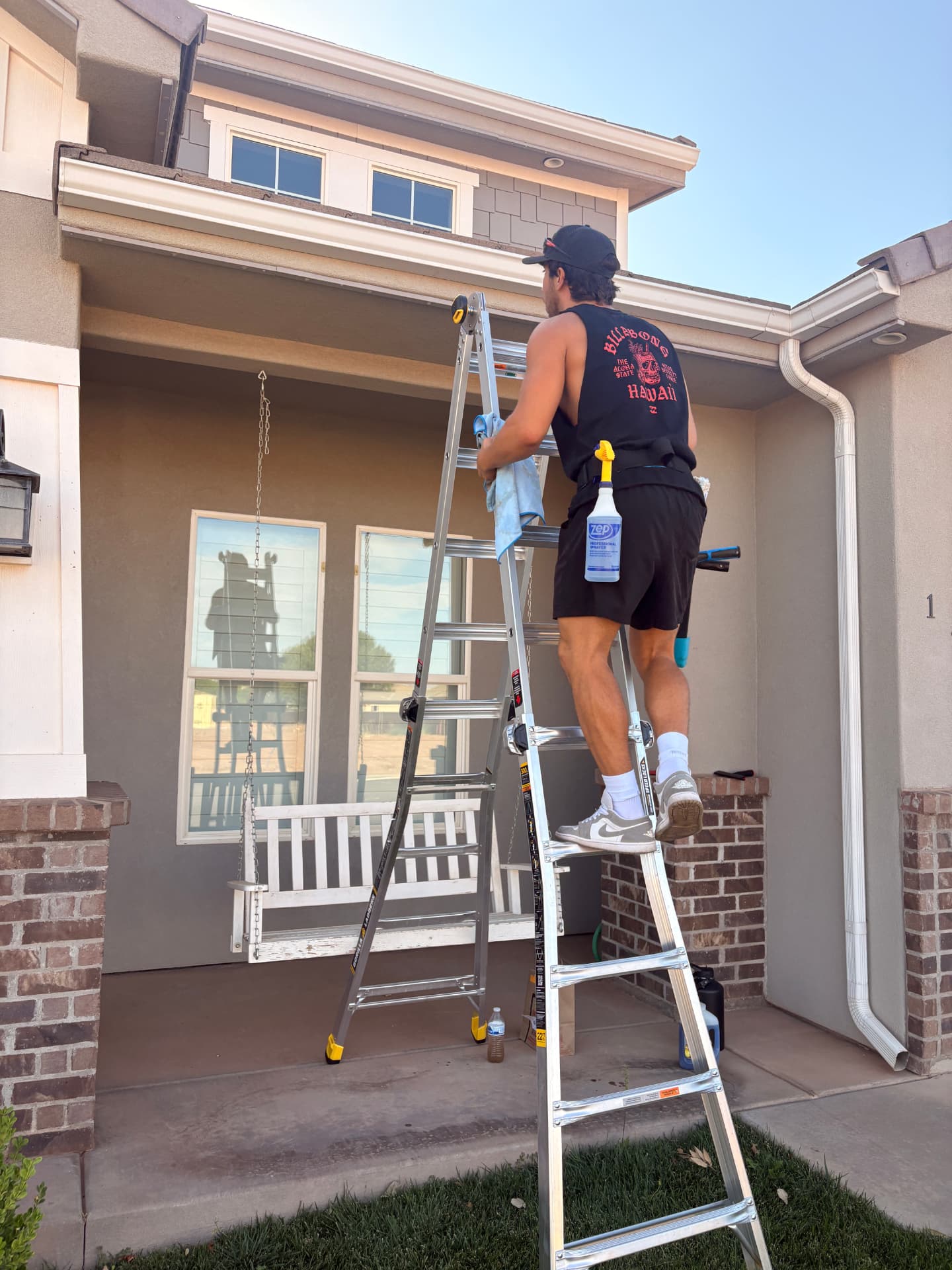 Window cleaner on a ladder cleaning upper windows of a home